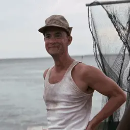 A Man Wearing A Hat And A Tank Top Is Standing On The Beach