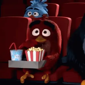An Angry Bird Is Sitting In A Theater Holding A Tray Of Popcorn And A Cup Of Soda