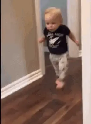 A Baby Is Walking Through A Doorway On A Hardwood Floor .
