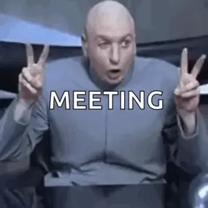 A Bald Man Is Sitting In A Chair Giving A Peace Sign And The Word Meeting Is Behind Him .