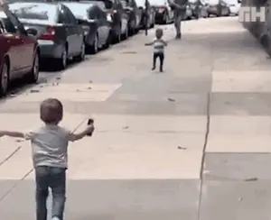 A Little Boy Is Walking Down A Sidewalk While Holding A Bottle Of Water .