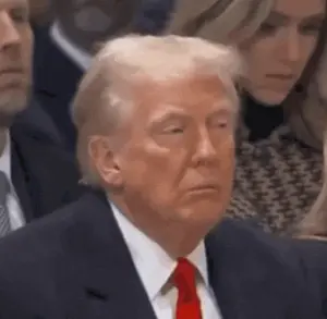 Donald Trump In A Suit And Tie Is Sitting In A Crowd Of People