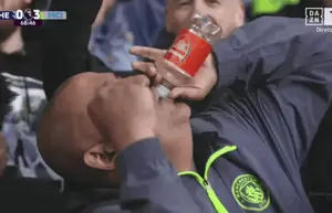A Man In A Manchester City Jacket Drinks From A Bottle