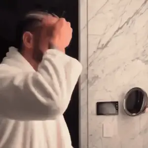 A Man In A White Robe Looks At Himself In The Mirror