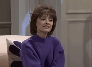 A Woman In A Purple Sweater Sits On A White Couch