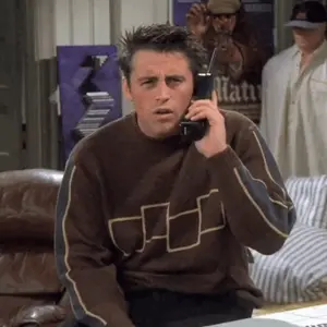 A Man In A Brown Sweater Is Talking On A Phone