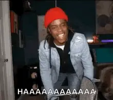 A Man Wearing A Red Hat And A Denim Jacket Is Holding A Skateboard .