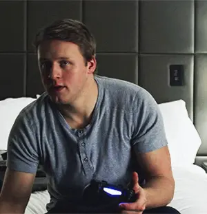 A Man Is Sitting On A Bed Playing A Video Game
