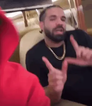 A Man With A Beard Is Sitting Next To Another Man In A Red Hoodie And Making A Peace Sign With His Hands .