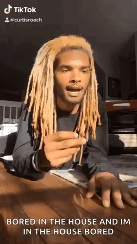 A Man With Dreadlocks Is Sitting At A Table Holding A Piece Of Paper And Making A Funny Face .