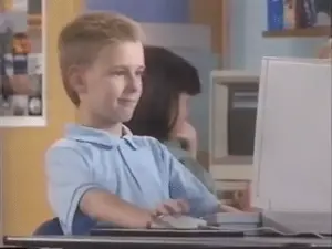 A Young Boy Is Sitting At A Desk Using A Computer