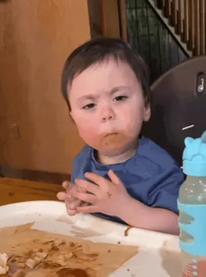 A Baby Sitting In A High Chair With Food On His Face And A Bottle Of Water