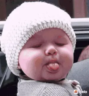 A Baby Wearing A Knitted Hat Is Sticking Out His Tongue .