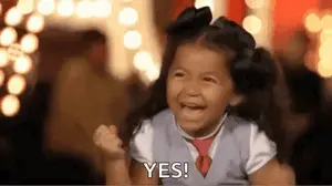 A Little Girl Is Smiling And Holding Her Fist In The Air While Saying Yes .