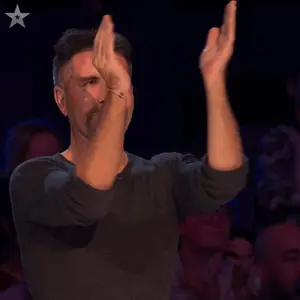 A Man With A Beard Applauds In Front Of A Crowd With A Star In The Corner