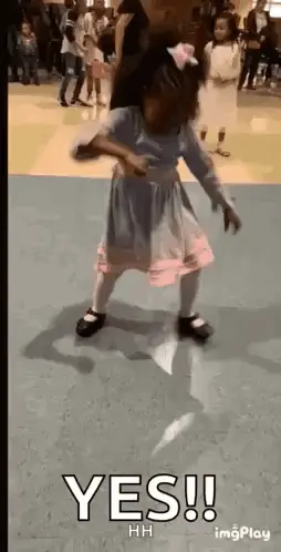 A Little Girl In A Dress Is Dancing On A Dance Floor In A Gym .