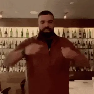 A Man With A Beard Is Dancing In Front Of A Wall Of Bottles .