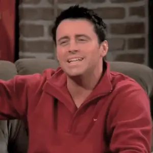 A Man Wearing A Red Nike Sweater Smiles While Sitting On A Couch
