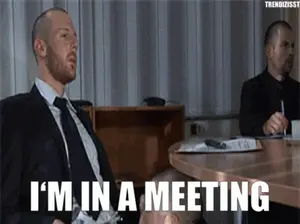 A Man In A Suit And Tie Is Sitting At A Table And Saying I 'M In A Meeting