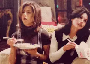 Two Women Are Sitting At A Table Eating Food With Chopsticks