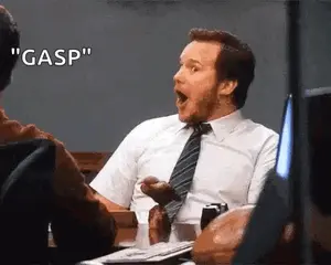 A Man In A Suit And Tie Is Sitting At A Table With His Mouth Open And A Surprised Expression On His Face .