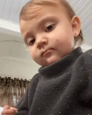 A Baby In A Black Sweater Is Making A Funny Face .