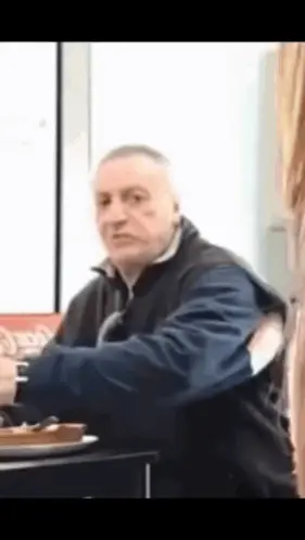 A Man In A Blue Jacket Is Sitting At A Table With A Plate Of Food .