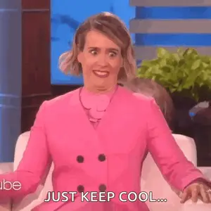 A Woman In A Pink Coat Is Sitting On A Couch Making A Funny Face And Saying `` Just Keep Cool '' .