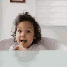 A Little Girl Is Sitting In A Bathtub And Smiling