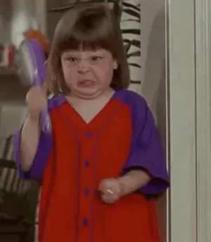 A Little Girl In A Red And Purple Dress Is Brushing Her Hair With A Brush .