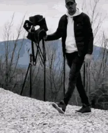 A Man Is Walking Down A Snowy Hill With A Camera .