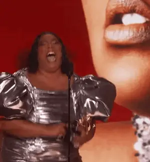 A Woman In A Silver Dress Is Singing Into A Microphone In Front Of A Red Background .