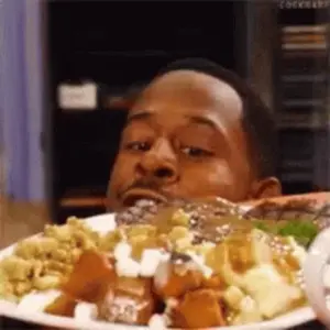 A Man Is Eating A Plate Of Food And Looking At The Camera .