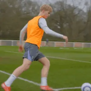 A Man Wearing An Orange Vest Is Kicking A Soccer Ball
