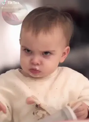 A Baby Is Making A Funny Face While Eating Food With A Spoon