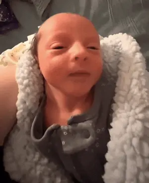 A Baby Is Wrapped In A White Blanket And Looks At The Camera