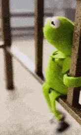 Kermit The Frog Is Sitting On A Wooden Railing