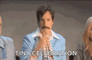 A Man With A Mustache In A Blue Suit Says Tiny Celebration In Front Of A Group Of People