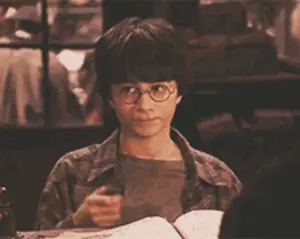 Harry Potter Is Holding A Wand While Sitting At A Table With A Book