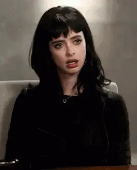 A Woman With Black Hair And Bangs Is Sitting At A Table With Her Mouth Open .