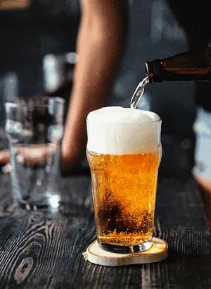 A Bottle Of Beer Is Poured Into A Glass On A Wooden Table