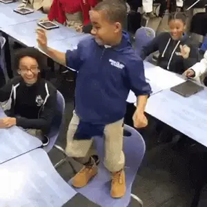 A Young Boy Is Dancing In A Classroom While Sitting At A Table .