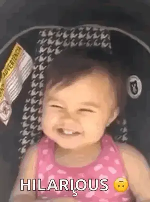 A Baby Girl Is Sitting In A Car Seat And Smiling With The Words Hilarious Written Next To Her .