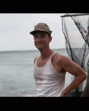 A Man Wearing A Hat And A Tank Top Is Standing In Front Of A Body Of Water