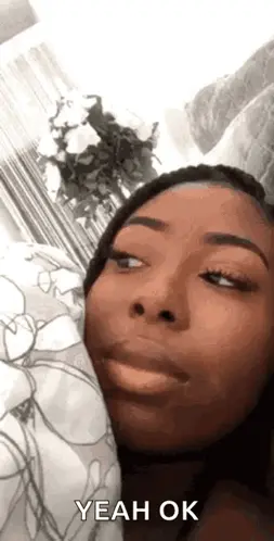 A Woman Is Laying In Bed With A Pillow And Making A Funny Face While Saying Yeah Ok .