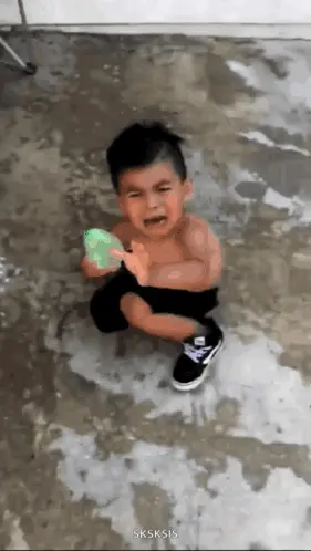 A Little Boy Is Crying While Holding A Green Water Balloon .