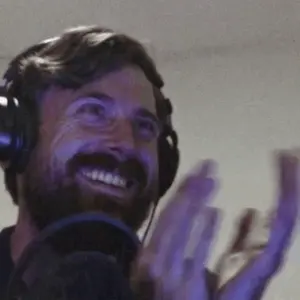 A Man With A Beard Wearing Headphones Is Smiling And Clapping