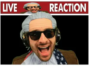 A Man Wearing A Wig And Headphones Stands In Front Of A Live Reaction Sign