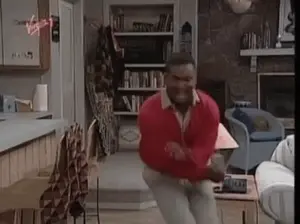 A Man In A Red Sweater Is Dancing In A Living Room In Front Of A Fireplace .