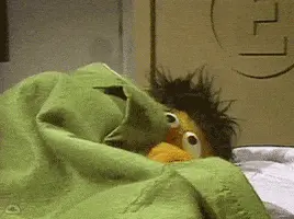 Ernie From Sesame Street Is Laying In Bed With A Green Blanket